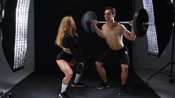 Athletic man and woman doing exercise on the shoulders with elastic bands on a black background in studio video