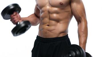 Man flexes his hands with dumbbells, training his shoulders on a white background in the studio video