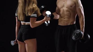 Athletic man and woman doing exercise on the shoulders with elastic bands on a black background in studio video