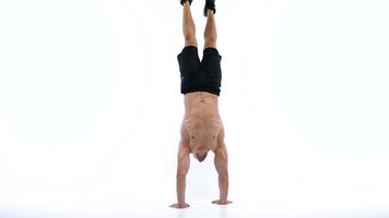 Man flexes his hands with dumbbells, training his shoulders on a white background in the studio video