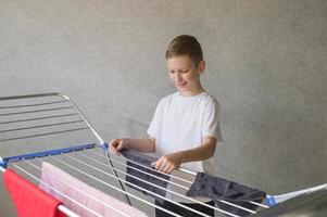 Cute boy hangs a wet towel on a metal clothes dryer, helps mom, housework, child's household chores photo