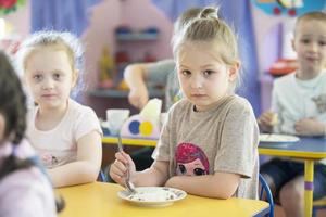 Children eat in kindergarten. Girl with a spoon at the table photo