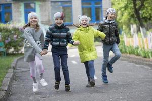 Happy preschoolers on the street. Children holding hands jumping. A group of six year old friends. photo