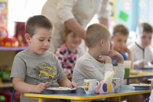 Children eat in kindergarten. Boy with a spoon and a plate at the table photo