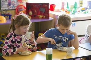 niños comer en jardín de infancia. niña y chico con un cuchara y un plato a el mesa foto