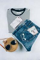 Flat lay with summer women's clothing and accessories. Striped t-shirt, blue denim shorts, fashionable organic rattan bag. Vacation, travel concept. Top view photo