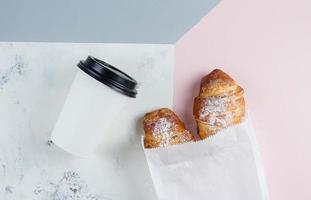 Fresco croissants con café a Vamos en un papel taza en tricolor antecedentes. tomar lejos desayuno. foto