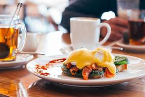 Poached egg on a piece of bread with salmon and spinach on the plate, mugs with coffee and tea photo