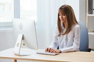 enfocado adorable rubia mujer de negocios trabajador persona de libre dedicación Mira a teclado pensando de problema solución en ligero moderno oficina. empleado trabajo en computadora en línea reflexionando o haciendo decisión. Copiar espacio foto