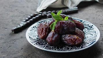 Ramadan kareem food concept. Fresh Dates, rosary beads and tea on dark concrete background photo