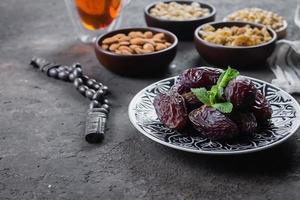 Ramadan Food Concept. Fresh Dates and nuts with rosery on dark concrete background. Ramadan kareem photo