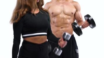 Athletic man and woman flexes their hands with dumbbells, training their biceps on a white background in studio video