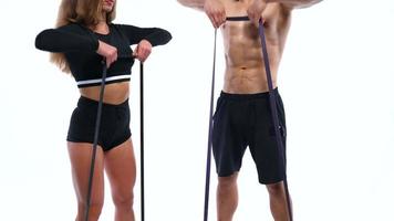 atlético hombre y mujer haciendo hombro ejercicios con elástico bandas en un blanco antecedentes en estudio video