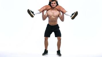 Athletic man crouches with a girl on his shoulders on a white background in studio video