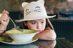Portrait of adorable little girl having lunch or dinner. Selective focus photo