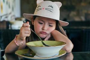 Portrait of adorable little girl having lunch or dinner. Selective focus photo