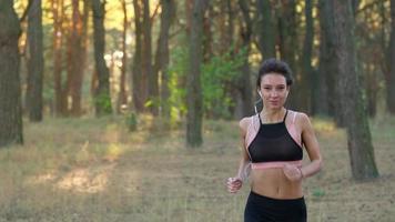 stänga upp av kvinna med hörlurar löpning genom ett höst skog på solnedgång video