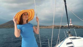 Woman in a yellow hat and blue dress girl rests aboard a yacht near the lighthouse on summer season at ocean video