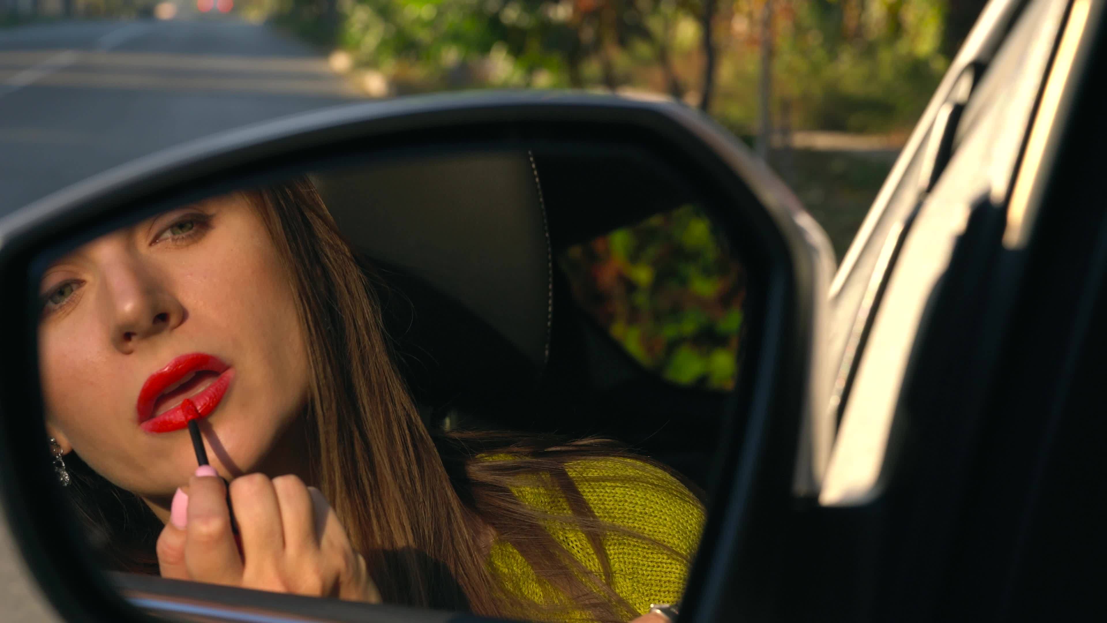 Woman paints her lips with red lipstick and looks in the rearview