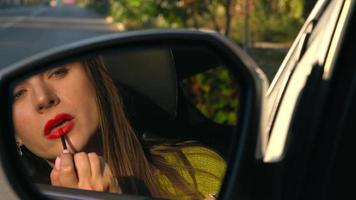 Woman paints her lips with red lipstick and looks in the rear-view mirror video