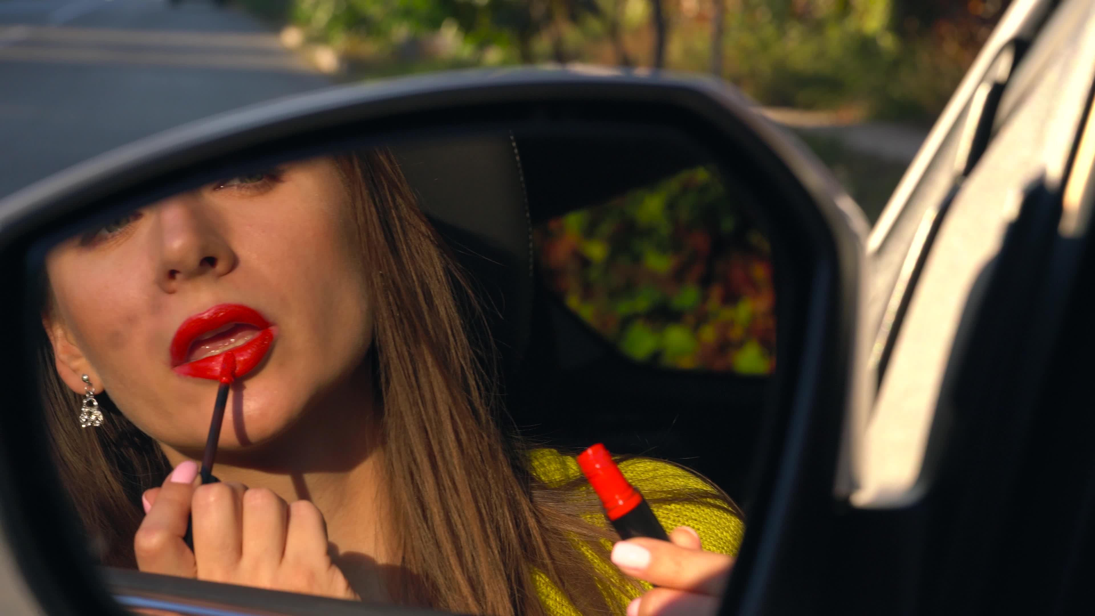 Woman paints her lips with red lipstick and looks in the rearview