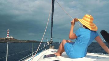 Frau im ein Gelb Hut und Blau Kleid Mädchen ruht an Bord ein Yacht in der Nähe von das Leuchtturm auf Sommer- Jahreszeit beim Ozean video