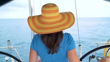 Woman in a yellow hat and blue dress girl rests aboard a yacht near the lighthouse on summer season at ocean video