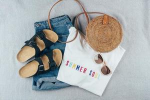 Flat lay with summer women's clothing and accessories. White t-shirt, denim shorts, rattan bag. photo