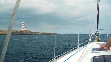 Woman in a yellow hat and blue dress girl rests aboard a yacht near the lighthouse on summer season at ocean video