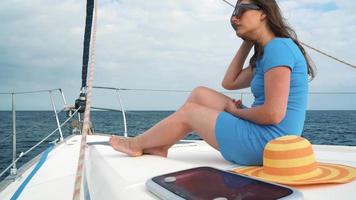 kvinna i en gul hatt och blå klänning flicka vilar ombord en Yacht nära de fyr på sommar säsong på hav video