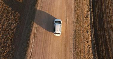 branco minivan carro lentamente drives em uma cascalho estrada entre a Campos às pôr do sol video