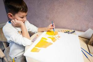 Left handed boy is painting by numbers with gouache at home. photo