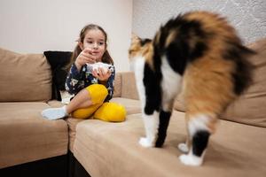 pequeño niña alimentar el gato con yogur desde un cuchara a hogar. foto