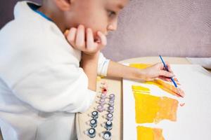 Left handed boy is painting by numbers with gouache at home. photo