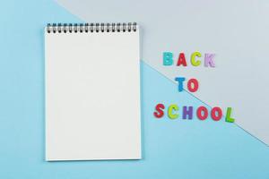 Top view of empty notebook, inscription by letters back to school on pastel background. photo