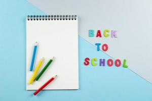 Top view of empty notebook with pencils, inscription by letters back to school on pastel background. photo