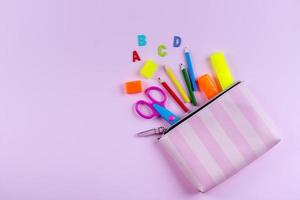 Back to school concept. School supplies in pencil case. Pink background with copy space. Flat lay photo