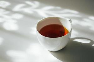 blanco taza de té en resumen antecedentes de natural cortina sombra que cae en blanco mesa. foto