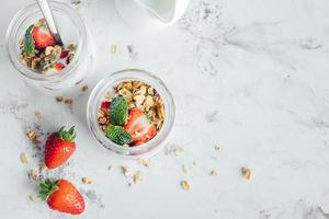 Summet tasty breakfast. Jars with parfaits made of granola, strawberries, yogurt on marble table photo