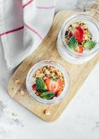 Two jars with tasty parfaits made of granola, strawberries and yogurt on marble table, top view photo