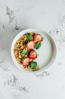 Healthy breakfast food minimal concept. Bowl with granola, yogurt and berries on white marble background. Top view, flat lay, copy space photo