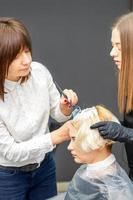 Two hairdressers dyeing hair of woman photo