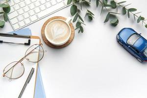 Modern white office desk table with laptop, notebook, toy car and other supplies. photo