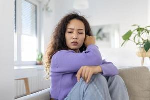 trastornado mujer frustrado por problema con trabajo o relaciones, sentado en sofá, cubierto cara en mano, sensación desesperación y ansiedad, soledad, teniendo psicológico problema foto