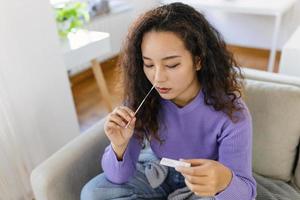 asiático mujer utilizando algodón torunda mientras haciendo coronavirus pcr prueba. mujer toma coronavirus muestra desde su nariz a hogar. mujer a hogar utilizando un nasal torunda para COVID-19. foto