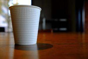 White Disposable Cup of Coffee on the Wooden Table in the Coffee Shop. photo