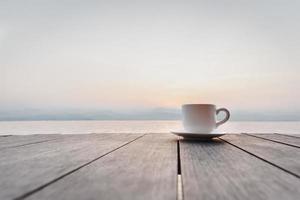 taza de café en de madera cubierta terminado amanecer con río montaña en antecedentes. foto