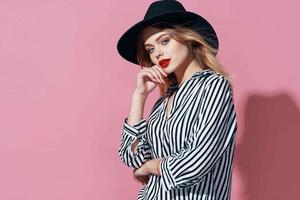 atractivo mujer en negro sombrero y a rayas camisa brillante maquillaje rosado antecedentes foto