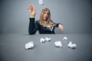 Funny millennial blonde businesswoman worker in blue jacket throws papers into the camera sitting at workplace in gray modern office. Tired of work Concept. Copy space, wide angle photo