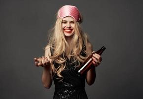 Woman with a bottle of beer on a gray background holidays sleep mask on her head photo